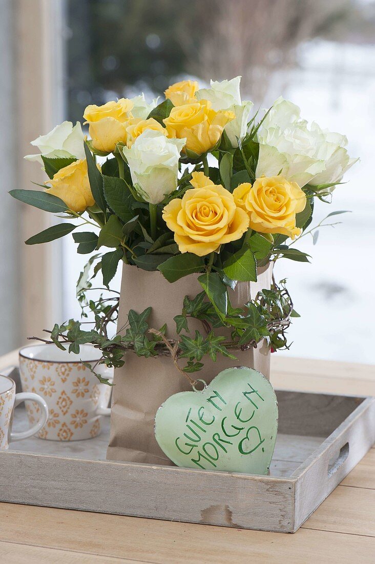 Yellow-white rose bouquet in paper bag with Hedera tendril