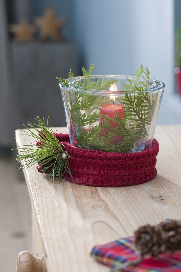Glas mit roter Kerze als Windlicht, dekoriert mit Thuja (Lebensbaum)