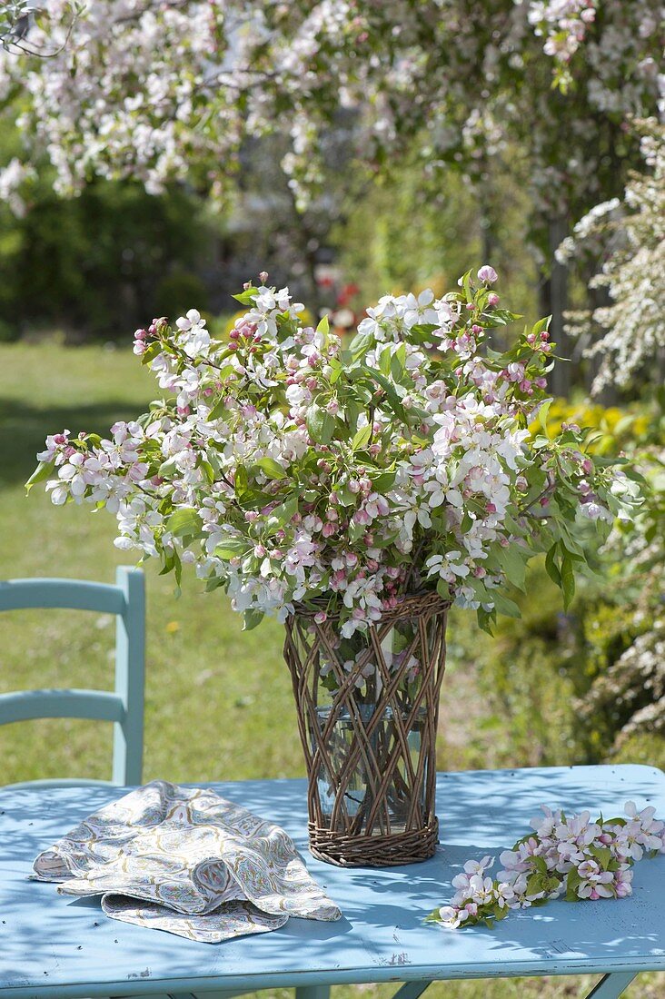 Malus (ornamental apple) branches bouquet in basket with glass vase