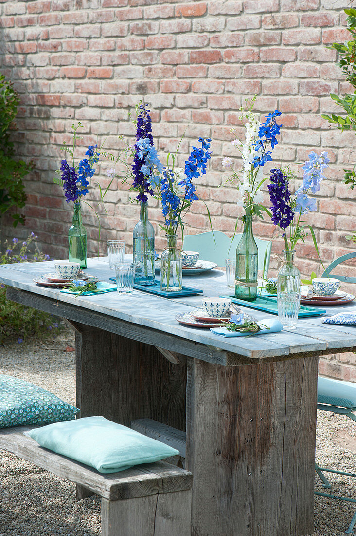 Gedeckter Tisch mit Delphinium (Rittersporn) in Flaschen