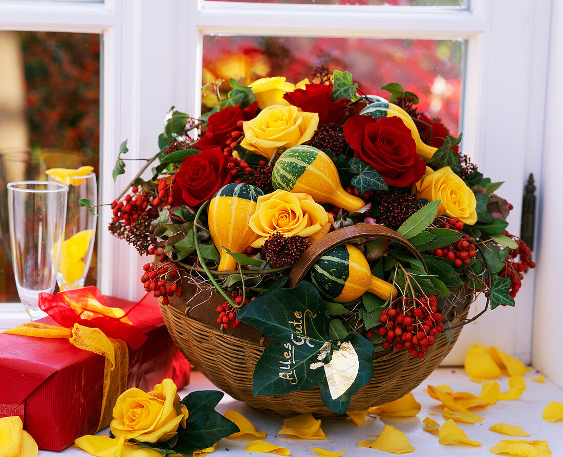 Basket with autumn arrangement of roses, ornamental gourds and berry decorations