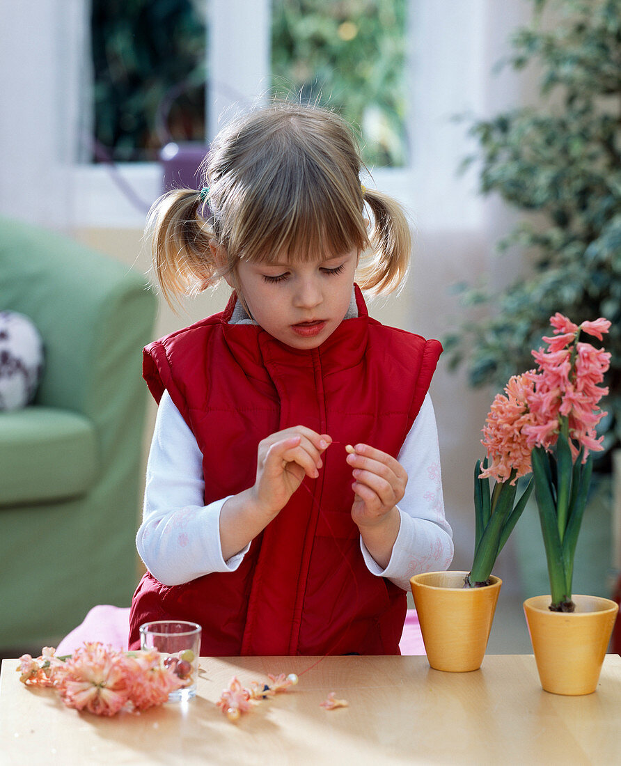Mädchen fädelt Hyacinthenblüten auf eine Perlenschnur