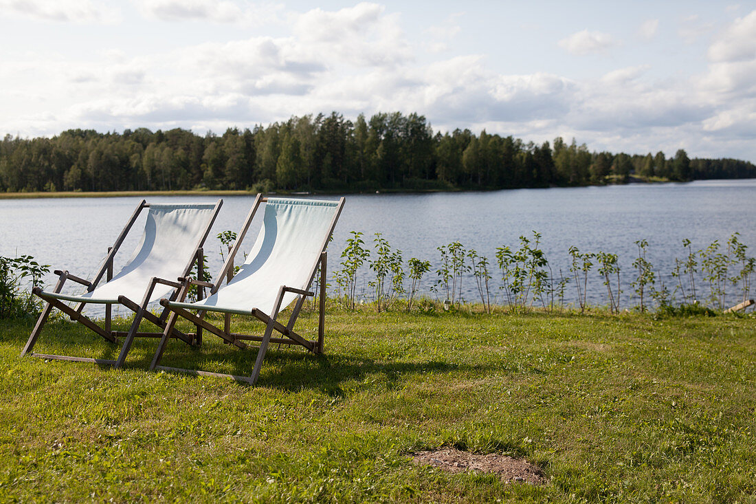 Two deckchairs on grass next to lake