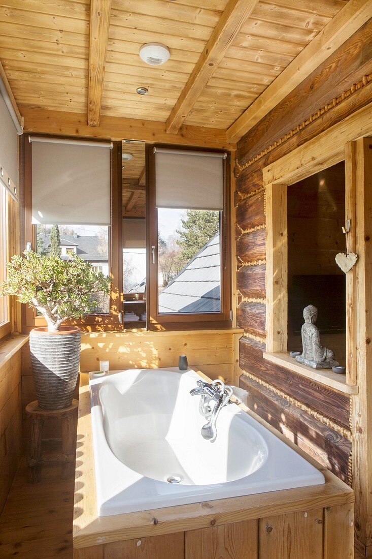 Wood-clad white bathtub below interior window in rustic dacha