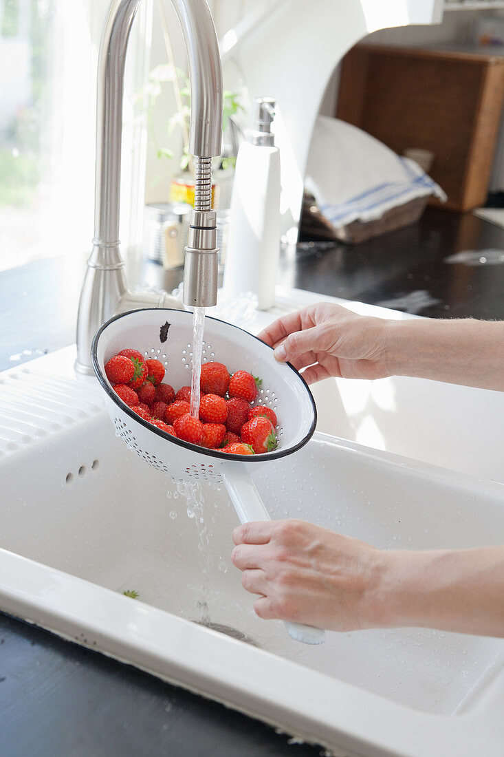 Hände waschen Erdbeeren im Küchensieb unter fließendem Wasser