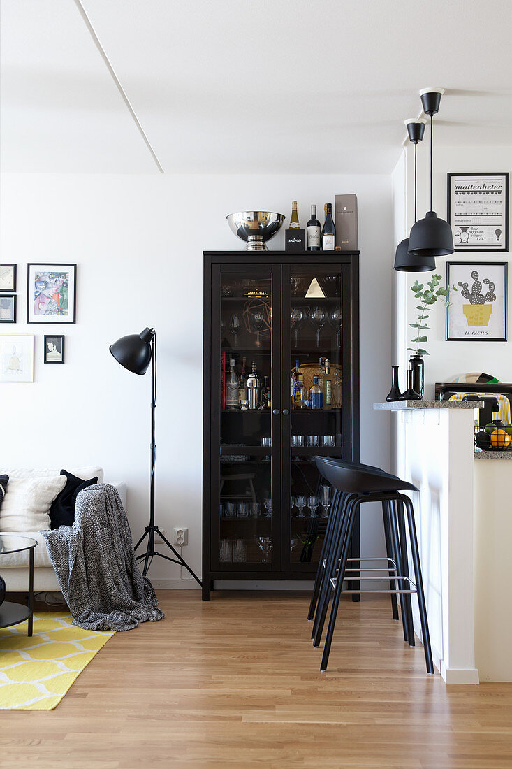 Barstools at partition kitchen counter and glasses in black glass-fronted cabinet