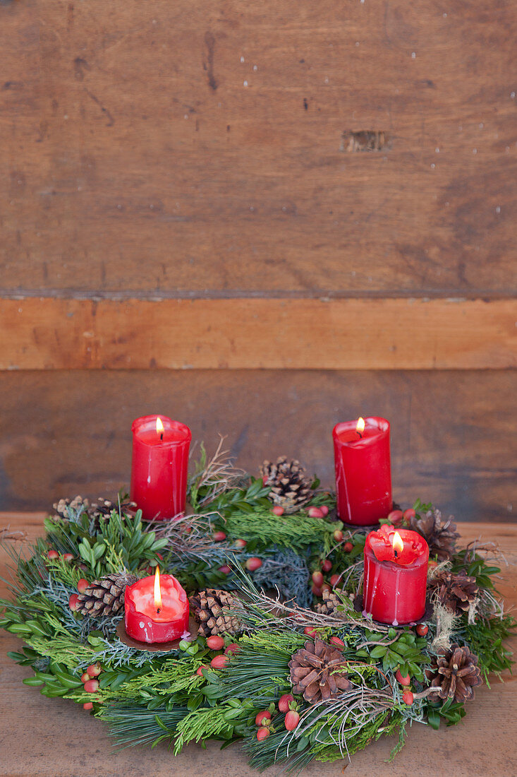 Lit red candles on Advent wreath against wooden wall