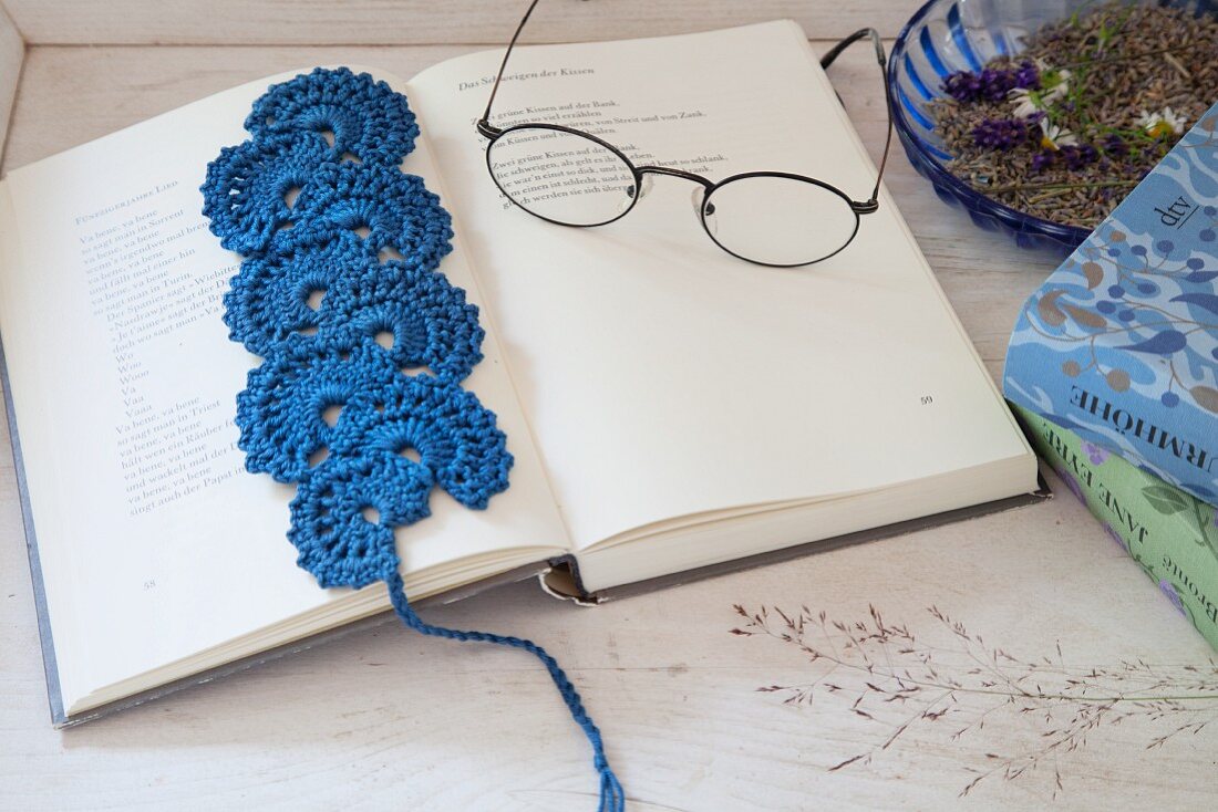 Blaues, gehäkeltes Lesezeichen und eine Brille auf dem Buch