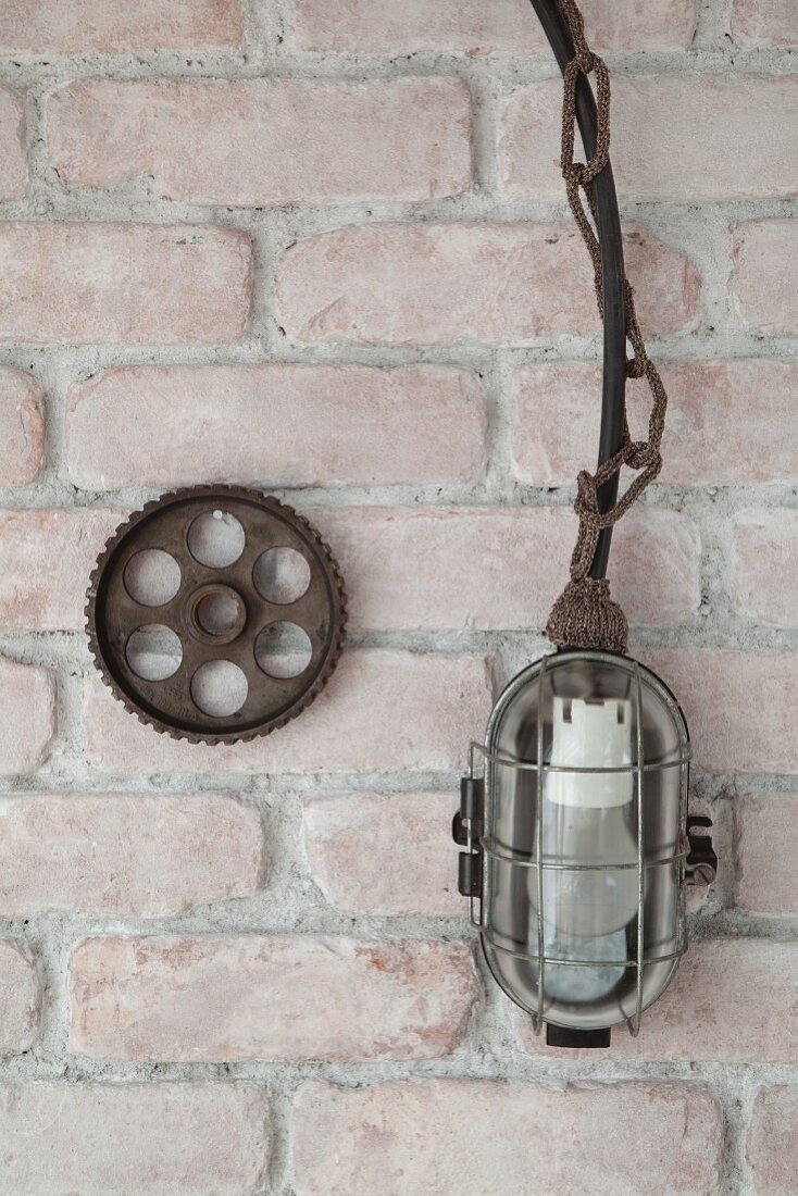 Werkstattlampe mit gestrickter Kette neben Zahnrad an Ziegelwand
