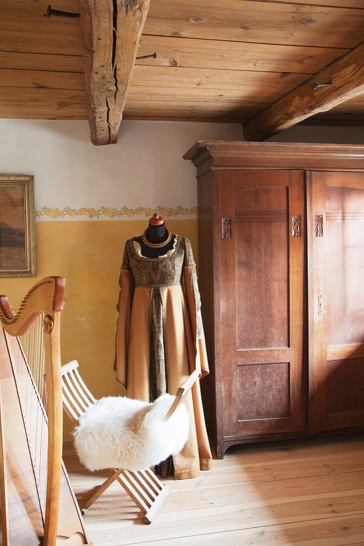 Historisches Gewand an Schneiderpuppe neben antikem Holzschrank, Stuhl mit Schaffell und Harfe
