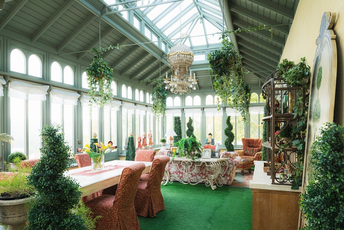 Green carpets and box hedge topiary in orangery with dining area and floral sofa