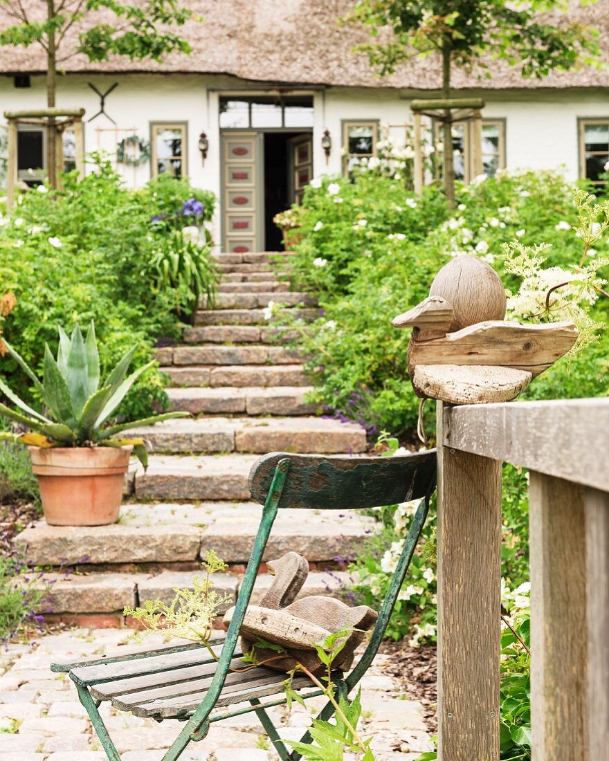 Vintage Gartenstuhl mit Holzente, Natursteintreppe vor friesischem Bauernhaus