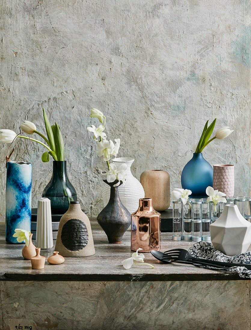 Verschiedene Vasen mit weißen Blumen vor einer Strukturwand