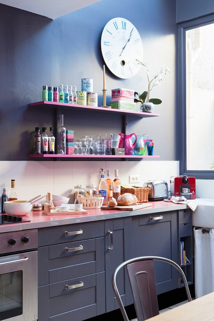 Pinkfarbene Regalbretter an dunkler Wand zwischen Wanduhr und Küchenarbeitsplatte