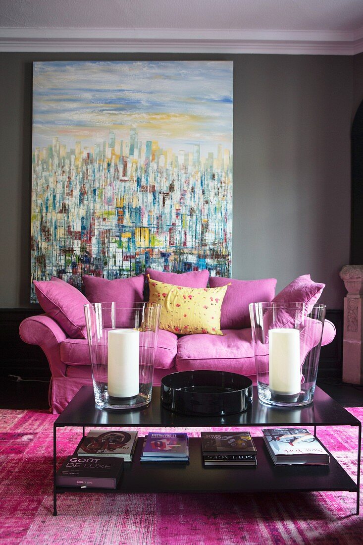 Pinkfarbene Couch mit Kissen und schwarzer Couchtisch vor Gemälde mit moderner Malerei