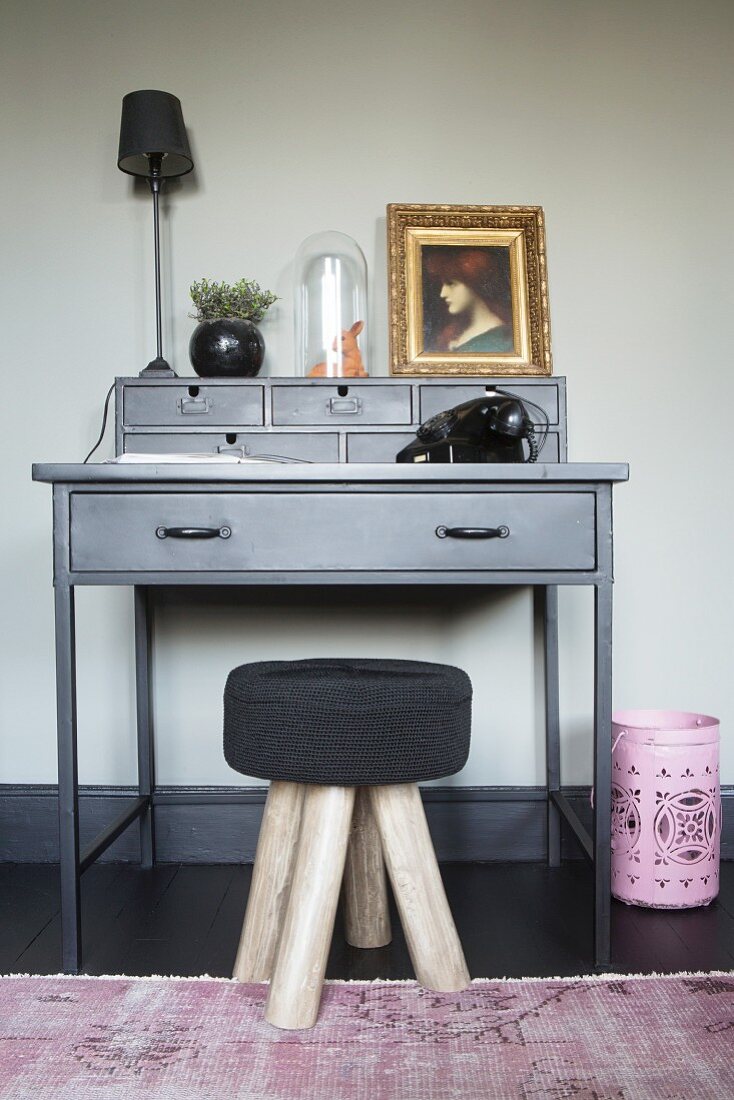 Black stool in front of vintage telephone and gilt-framed portrait of woman on grey writing desk