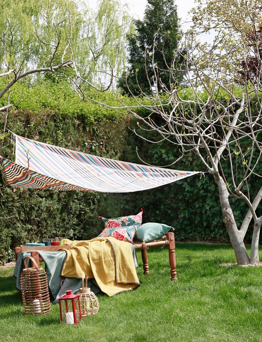 Comfortable lounger under striped awning in garden