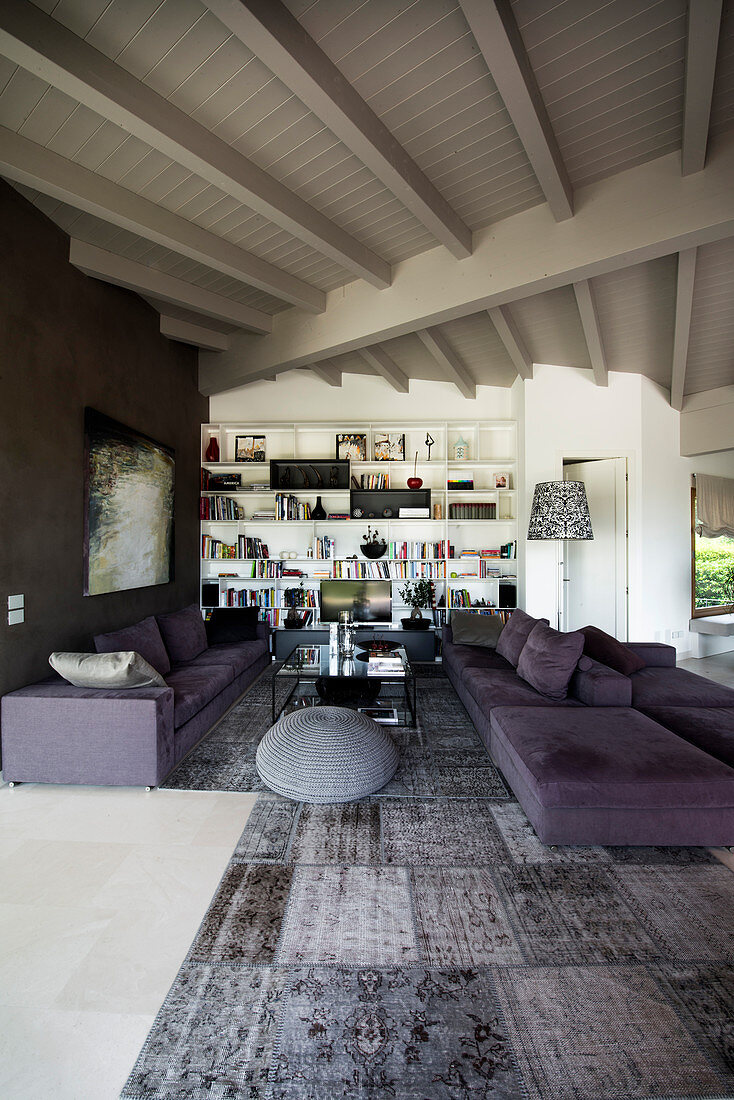Persesrteppich in Grautönen und lila Polstergarnitur in offenem Wohnraum mit weiß gestrichener Holzdecke