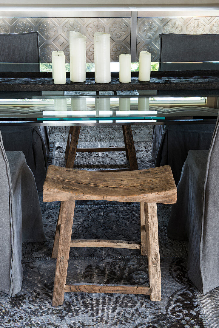 Rustikaler Holzschemel am eleganten Glastisch mit Kerzendeko