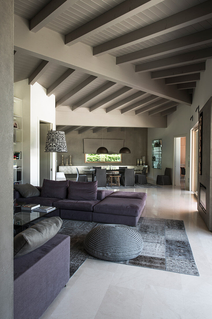 Persian rug in shades of grey and sofa set in open-plan interior with white-painted wooden ceiling