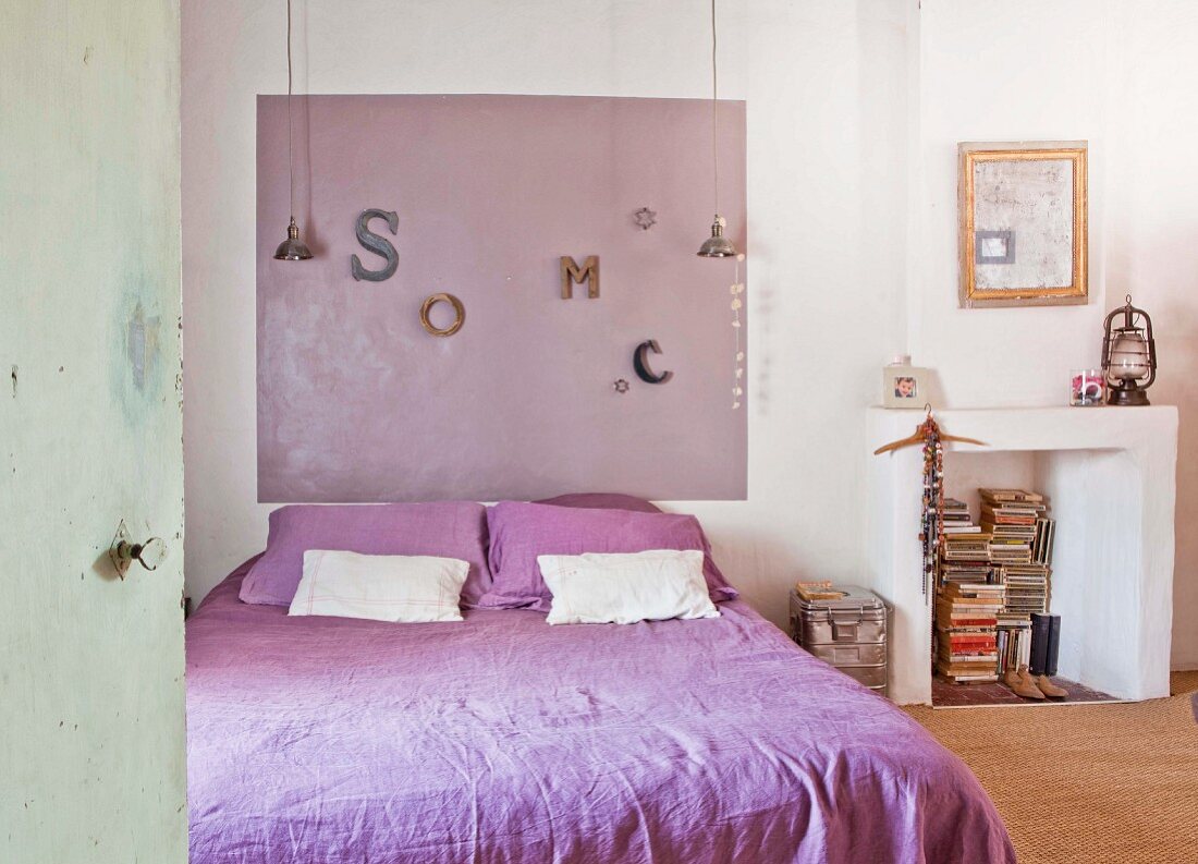 Double bed with purple bed linen, colour coordinated panel on wall and disused fireplace