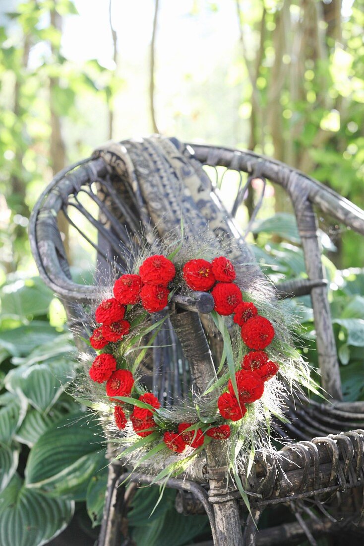 Roter Zinnienkranz aus Blütenköpfen und Rutenhirse an verwittertem Korbsessel