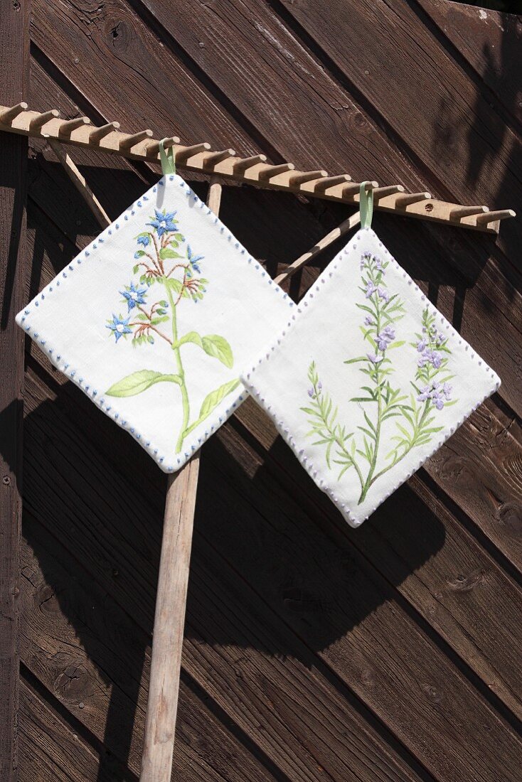 DIY-Topflappen mit aufgemalten und bestickten Blütenmotiven an Holzrechen