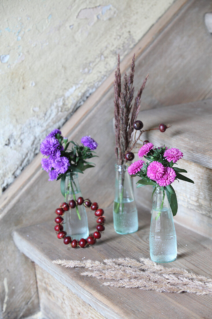 Astern und Herbstgräser in kleinen Glasflaschen und Hagebuttenkränzchen als Treppendekoration