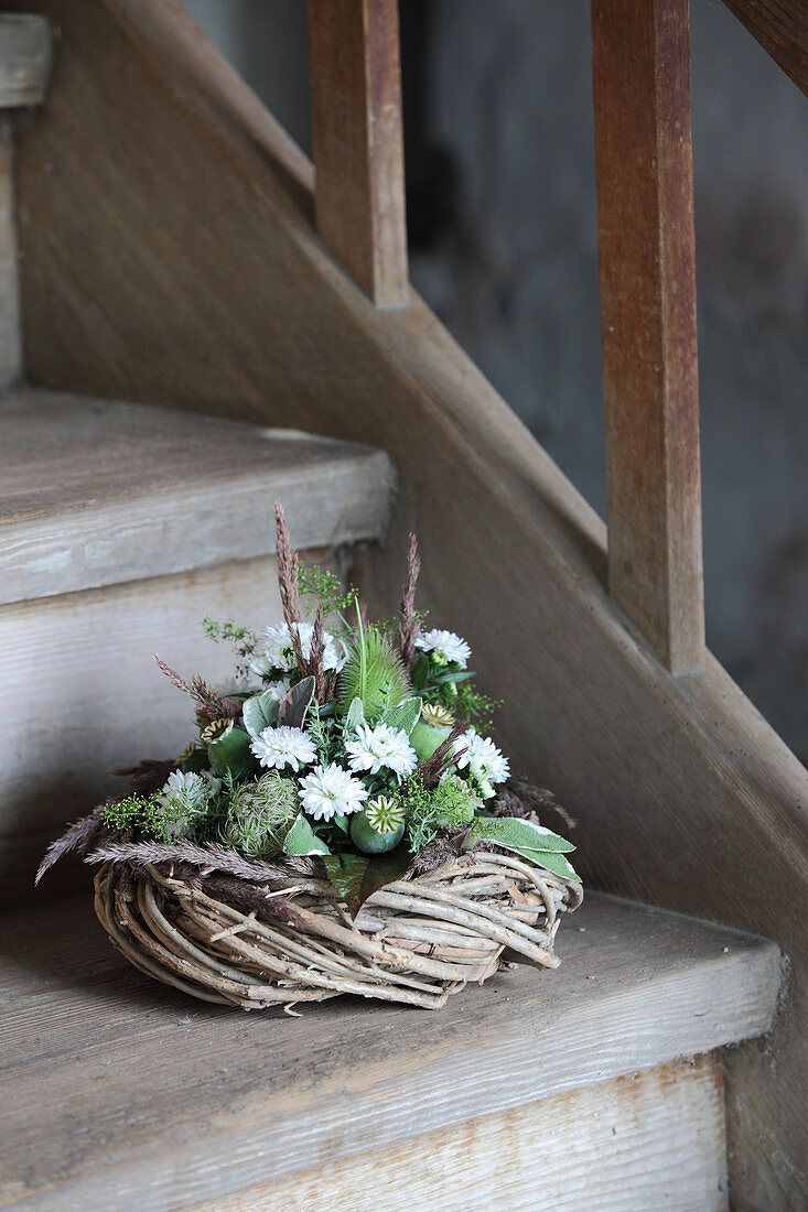 Wreath decorated with white asters and poppy seedheads on wooden staircase