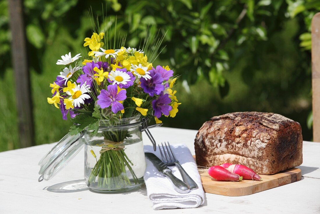Blumensträußchen im Einmachglas auf dem Tisch mit Brot