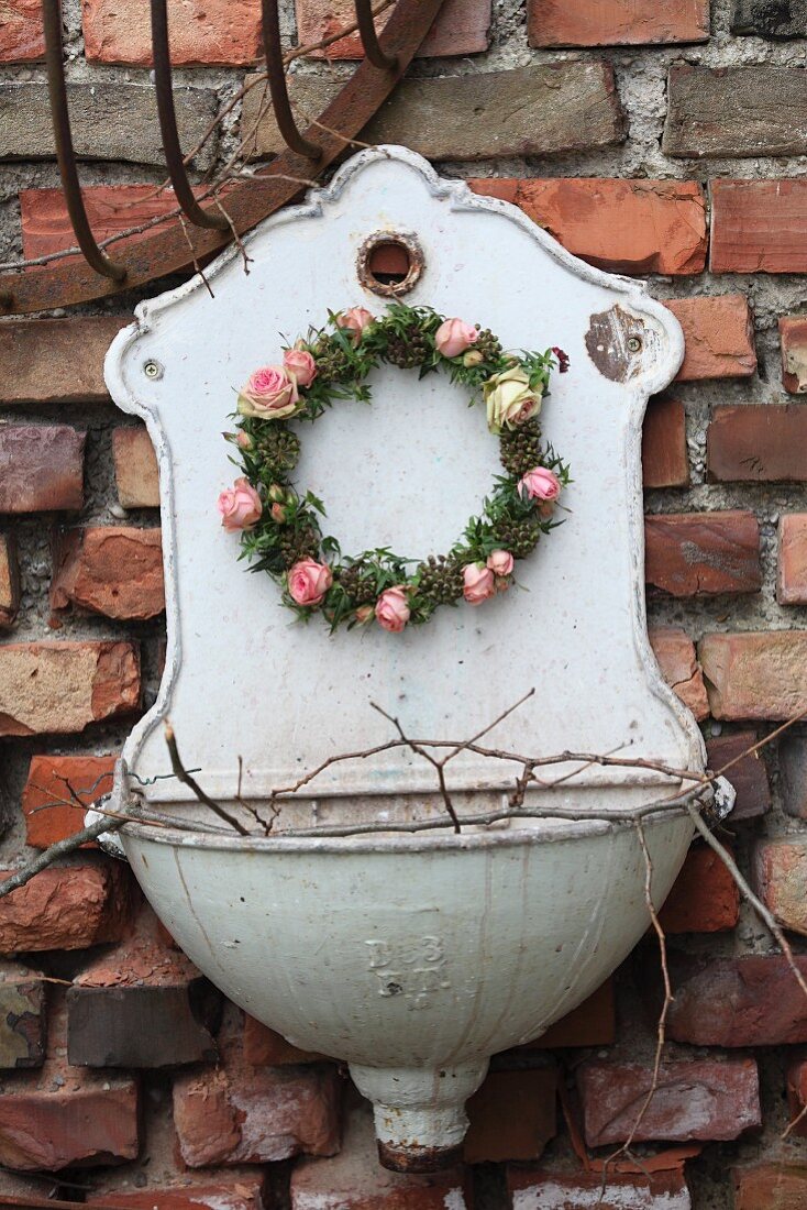 Romantischer Blütenkranz mit rosafarbenen Rosenblüten und Efeublättern an nostalgischem Waschbecken