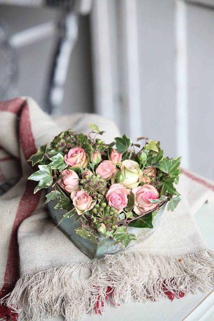 Romantisches Rosengesteck mit Efeu in herzförmigem Vintage Gefäß