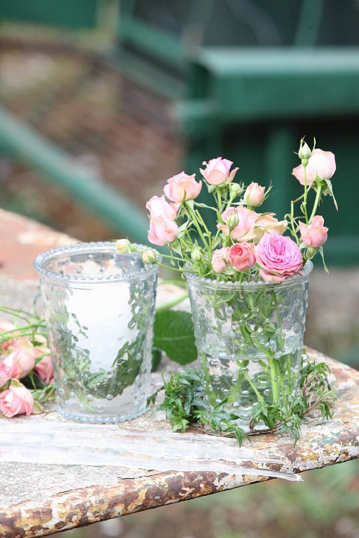 Romantisches Arrangement mit Rosenblüten und Kerze in zwei Glasgefäßen