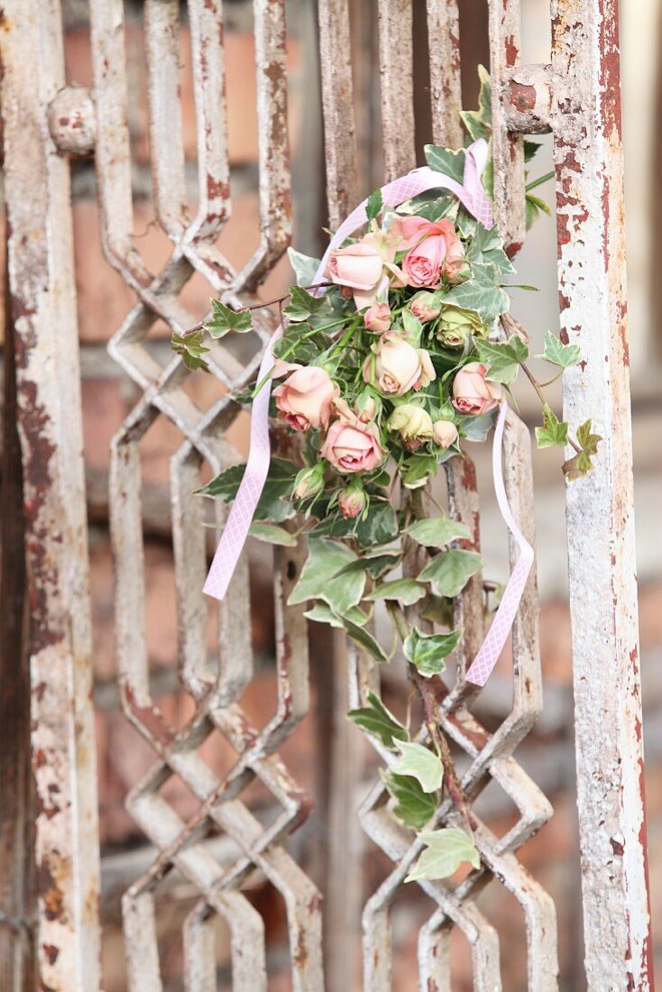 Romantischer Blumenstrauß mit Efeu und rosafarbenen Rosenblüten an Vintage Gitter