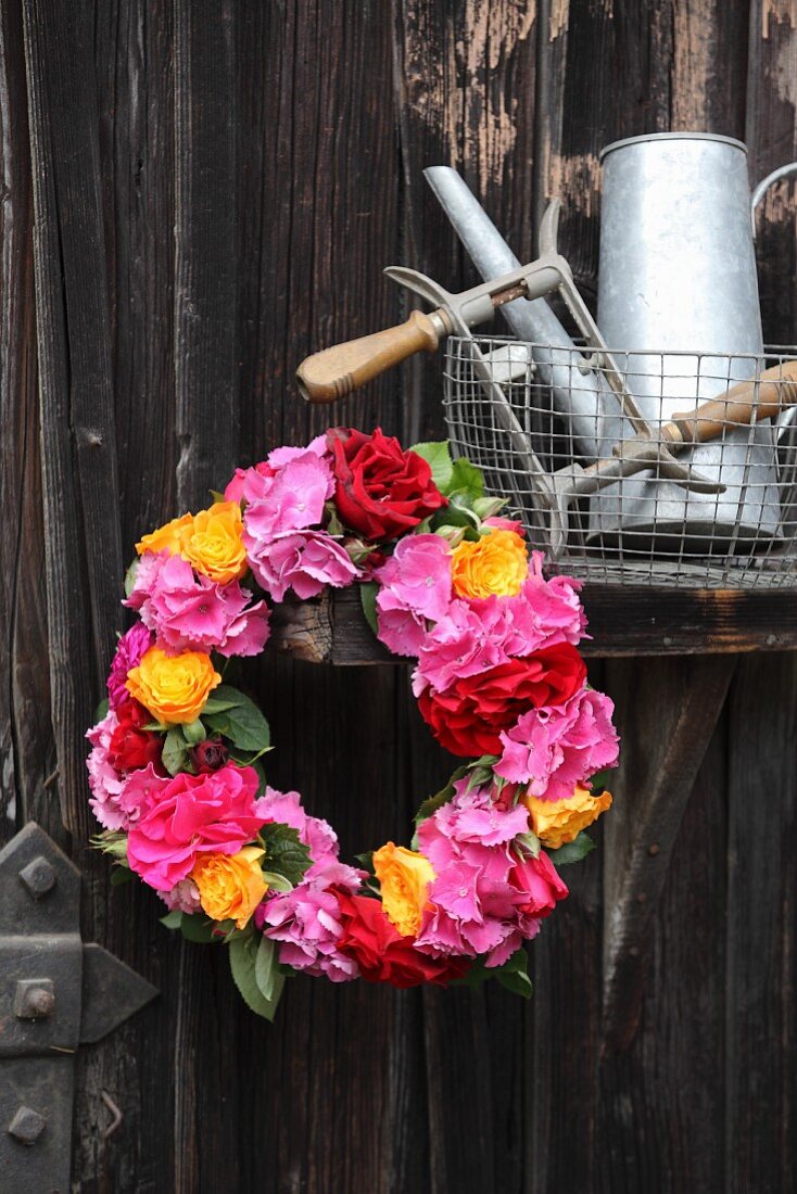 Wreath of hydrangeas and roses in shades of red and orange hung on old wooden door