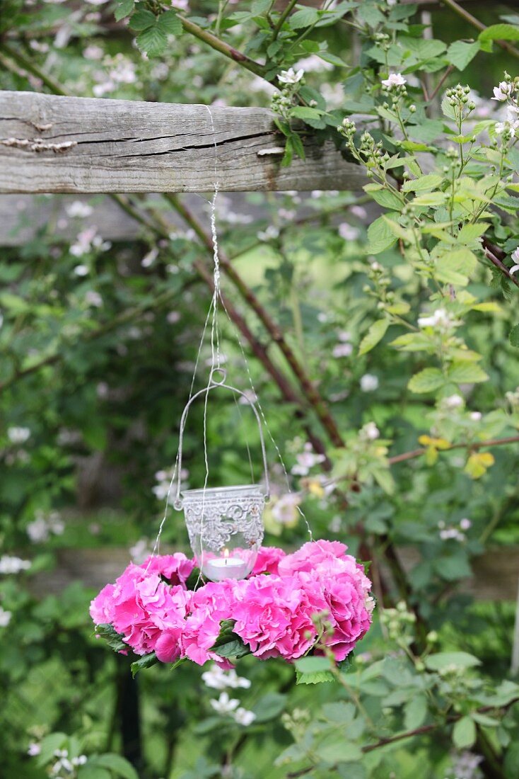 Candle lantern in wreath of pink hydrangeas hung from wooden beam
