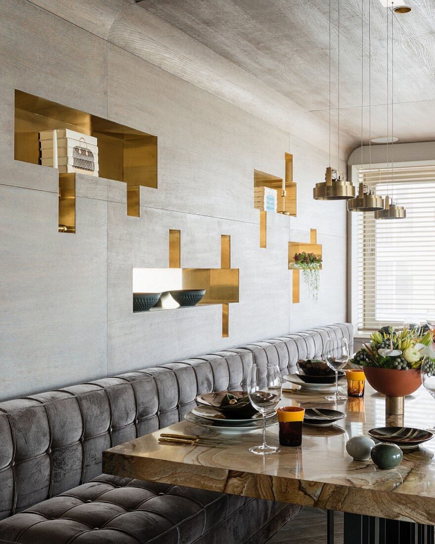 Gedeckter Esstisch mit edler Stone Wood Marmor Tischplatte vor grauer Holzverkleidung mit glänzenden, geometrischen Wandnischen
