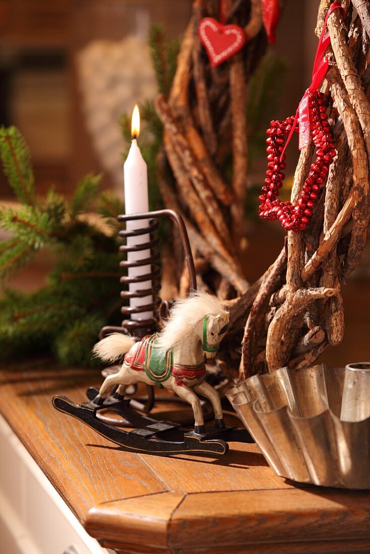 Christmas arrangement of rustic twig wreath, candle, rocking horse ornament and old bundt cake tin