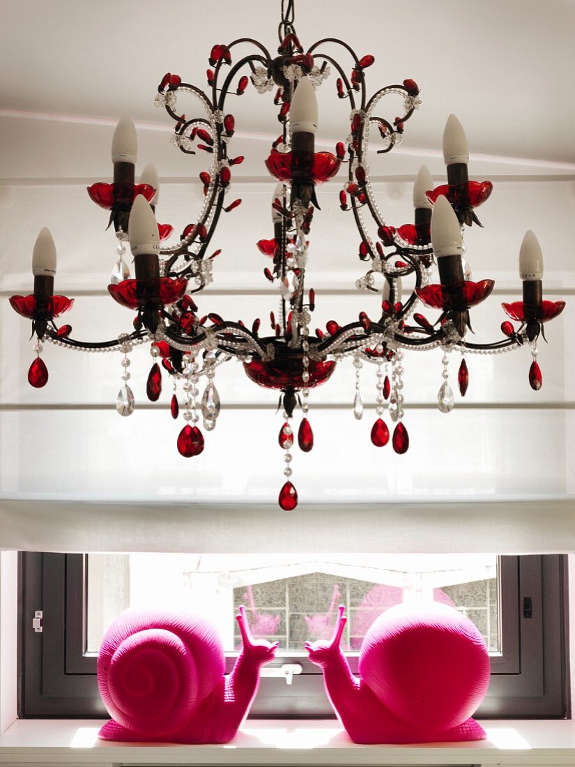 Two hot-pink, plastic snails on windowsill below romantic chandelier