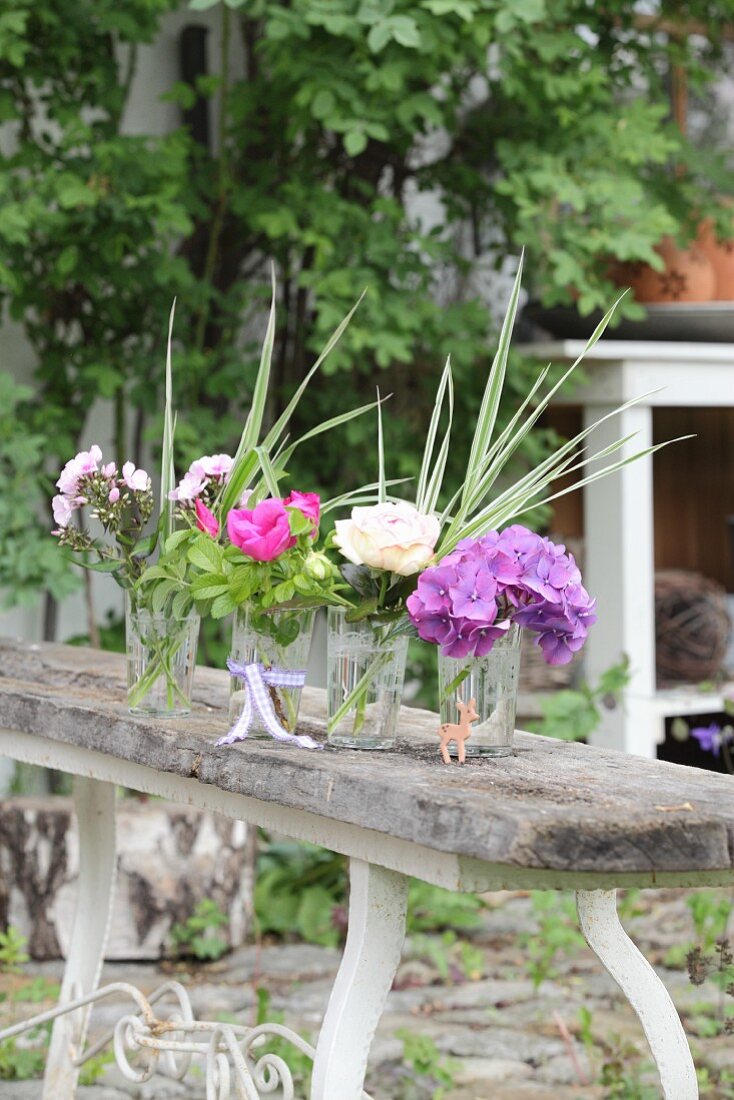 Various flowers in glasses of water on wooden bench
