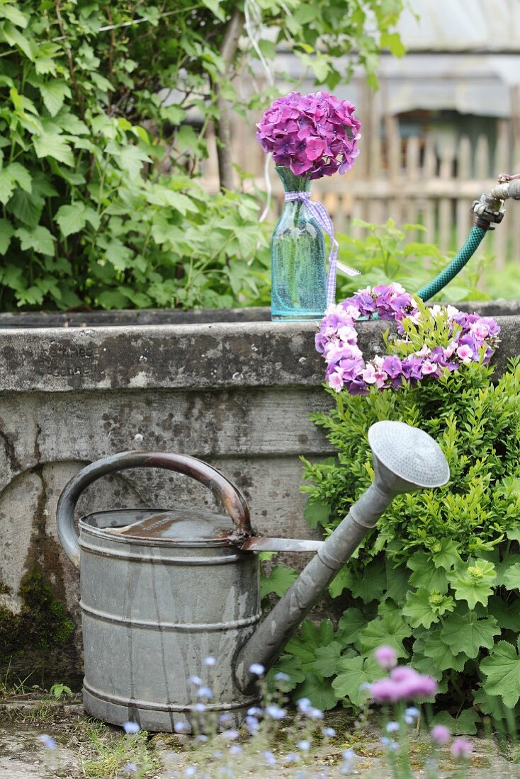 Zinc watering can in front of stone pool decorated with flowers