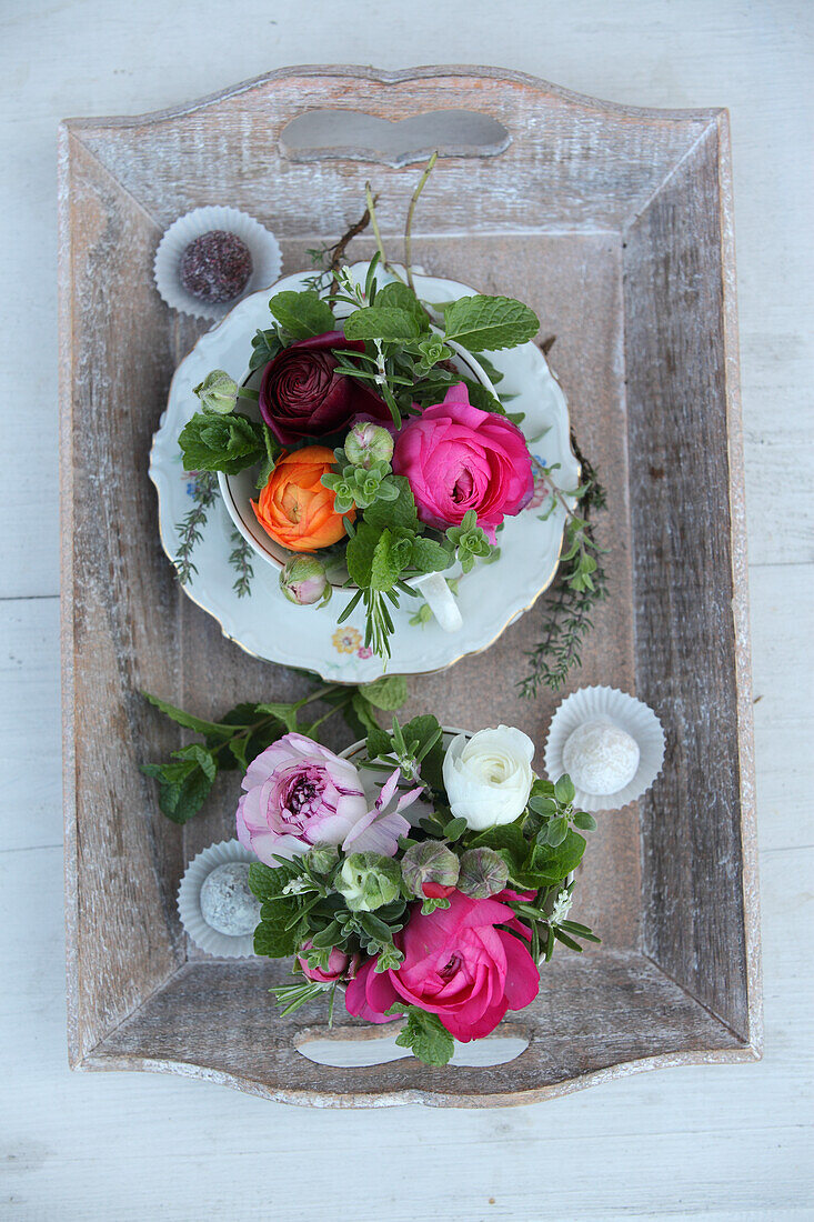 Colourful flower arrangements in old-fashioned teacups on wooden tray