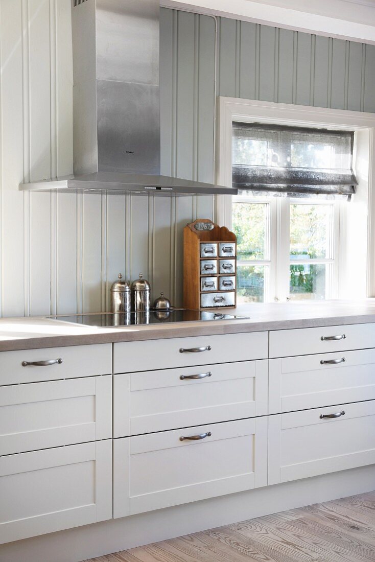 Extractor hood and wood-clad walls in white country-house kitchen
