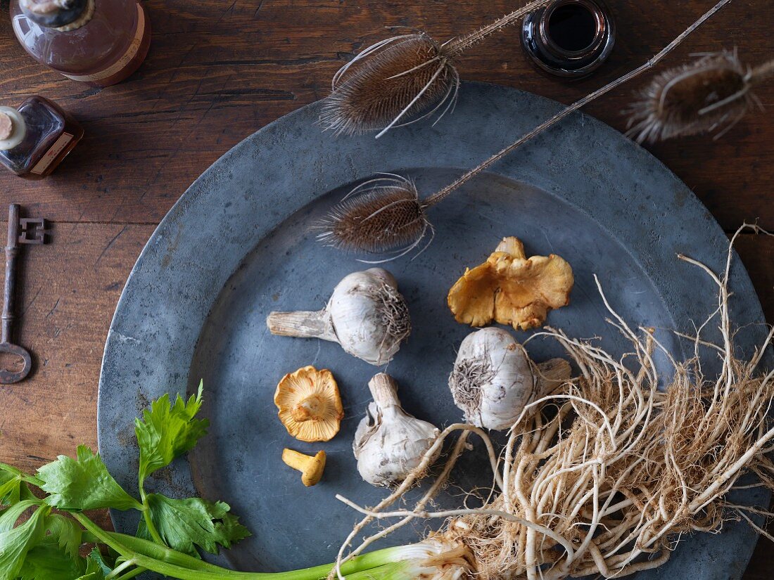 Sellerie, Pilze und Knoblauch auf Zinnteller, daneben getrocknete Rohkolben und Vintage-Flaschen