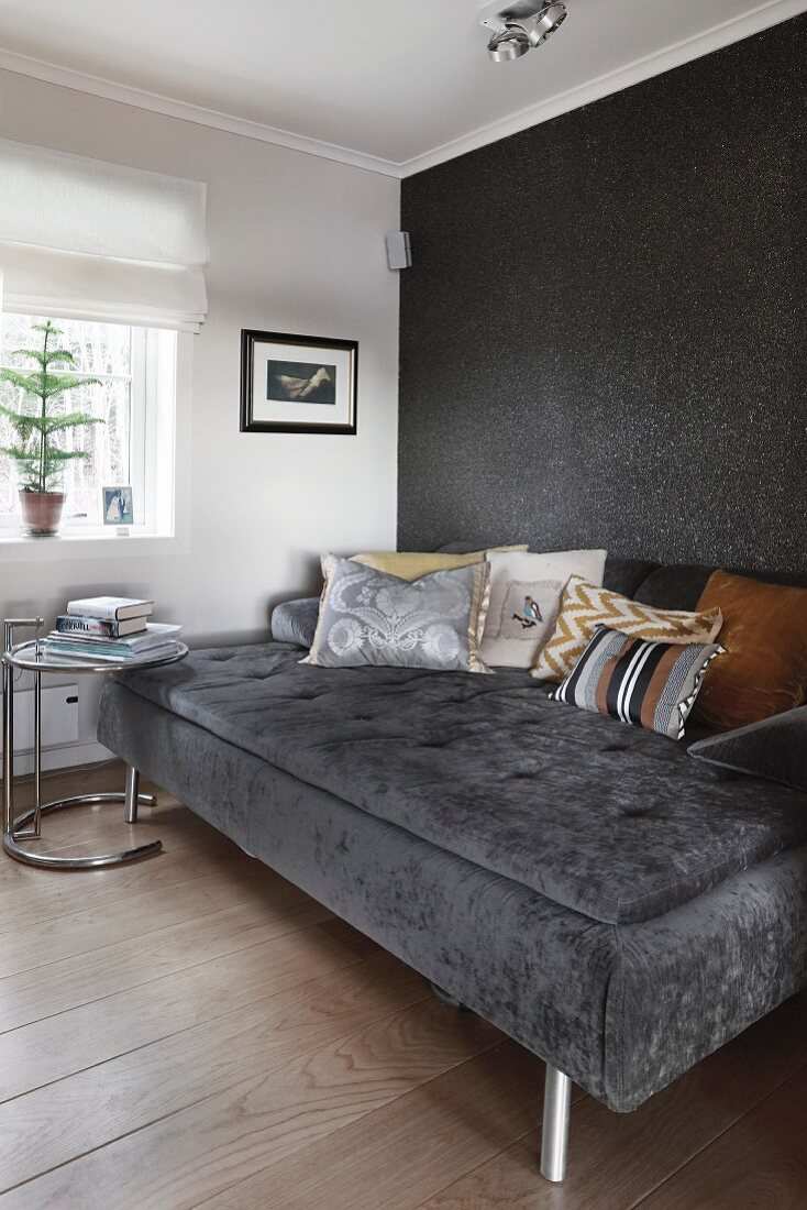 Breite Couch mit Kissen vor schwarzer Wand und Beistelltisch