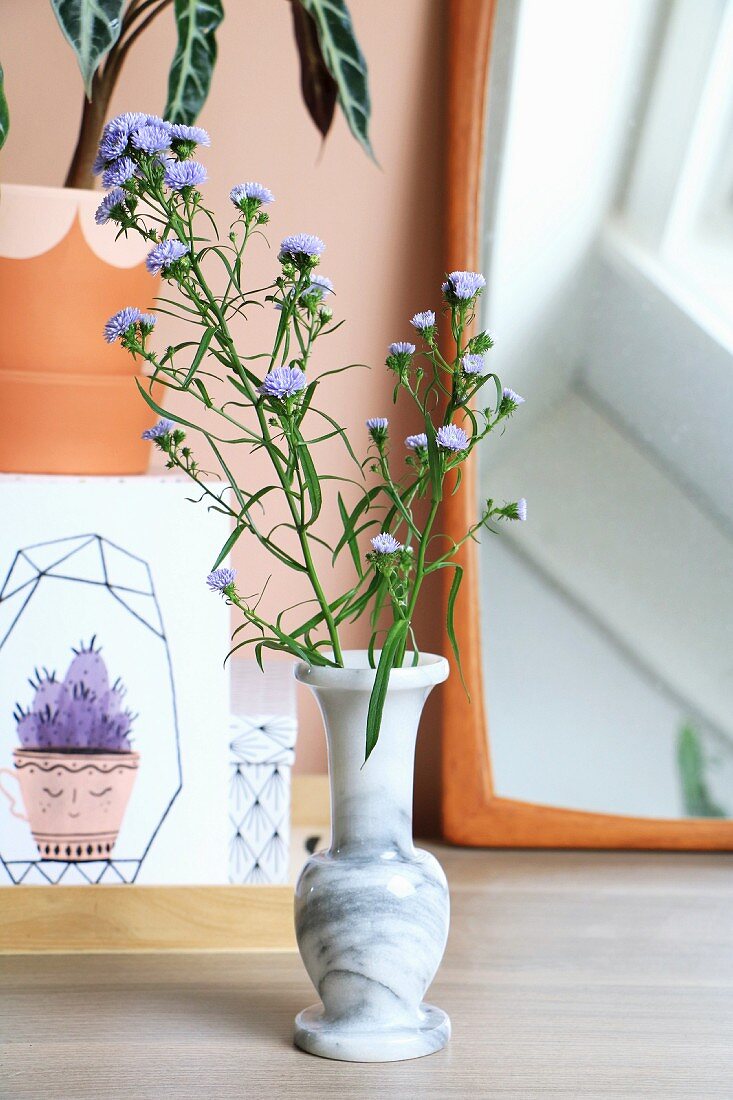 Marmorvase mit lila Blütenzweigen vor Spiegel und Zeichnung mit Kaktusmotiv