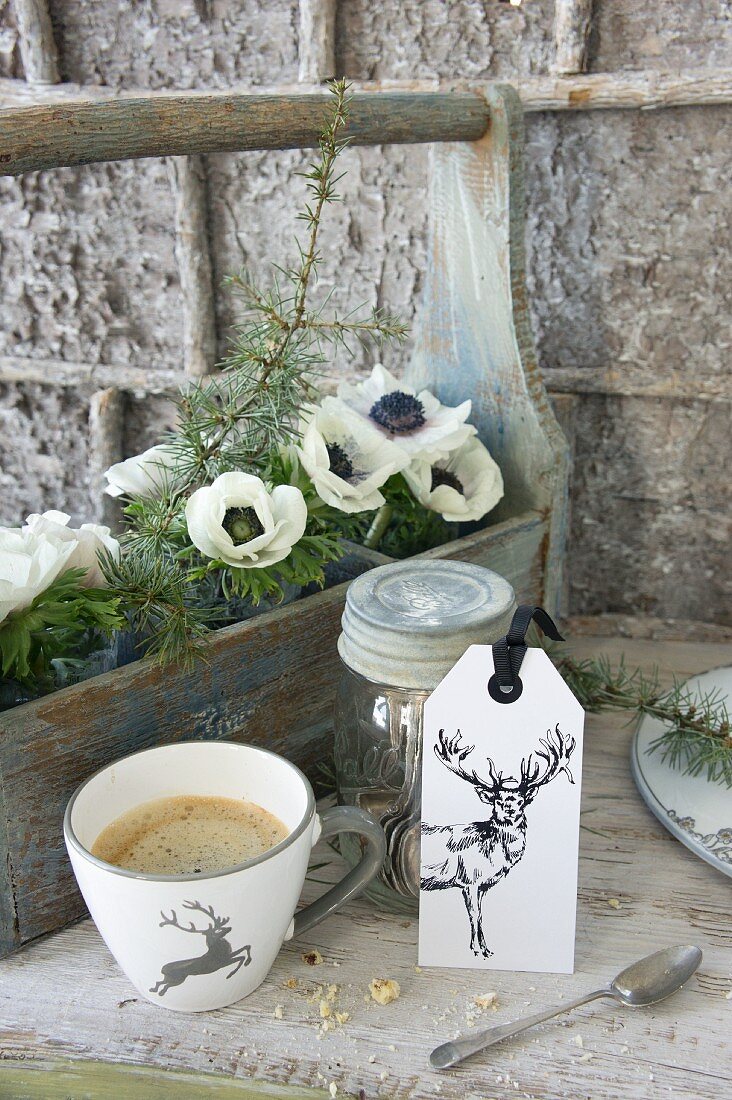 Tasse und Etikett mit Hirsch vor Flaschenträger mit weißen Anemonen