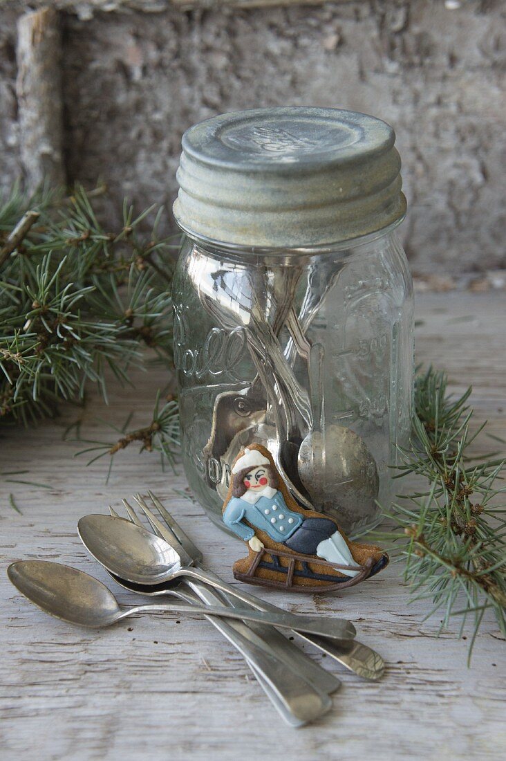 Iced biscuit shaped like boy on sledge leaning against screw-top jar holding silver cutlery