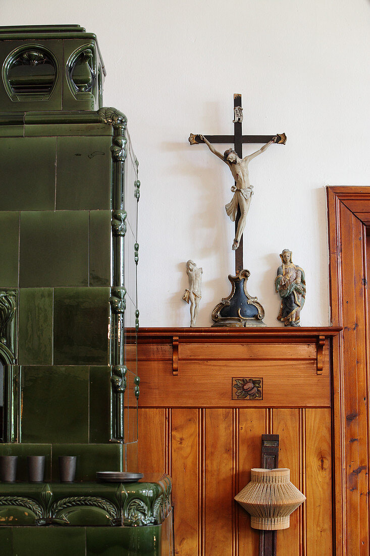 Crucifix on wooden shelf next to green tiled stove