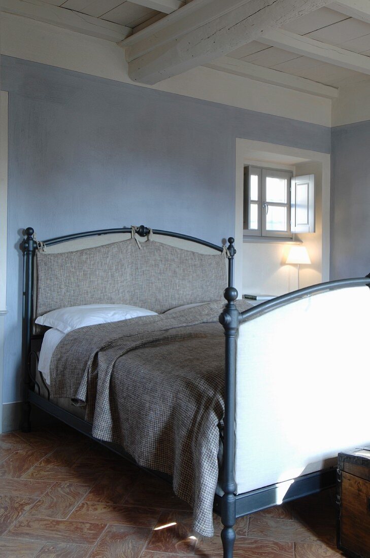 Doppelbett an taubenblauer Wand unter weiß gestrichener Holzbalkendecke